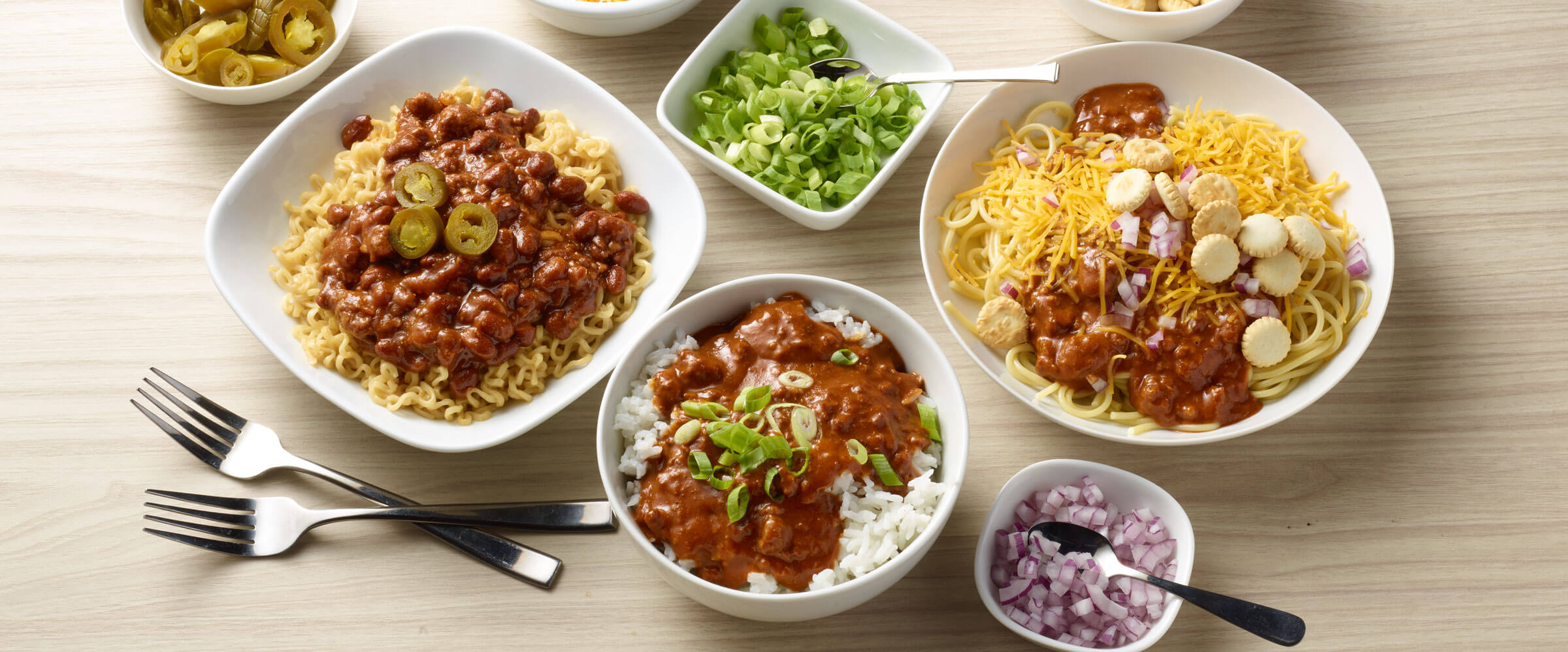 Chili 3 Ways with bowls of toppings including green onions, red onions, jalapenos and rice