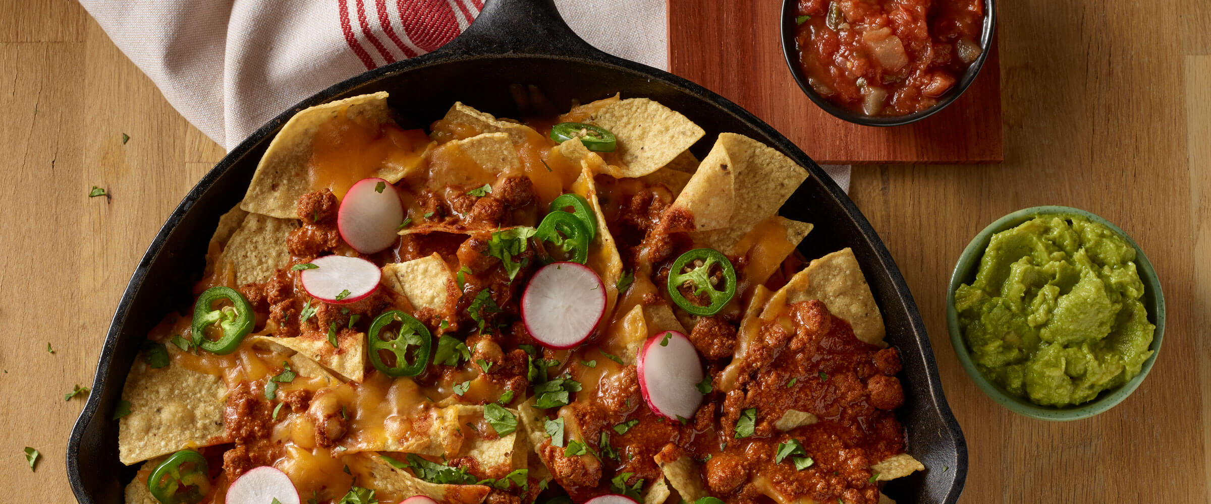 Skillet chili nachos in cast iron pan topped with cheese, radish and jalapenos with guacamole and salsa on the side