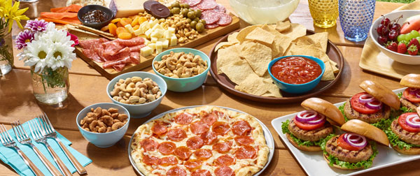 Summer themed picnic spread with pizza, snack nuts, charcuterie, burgers and snacks