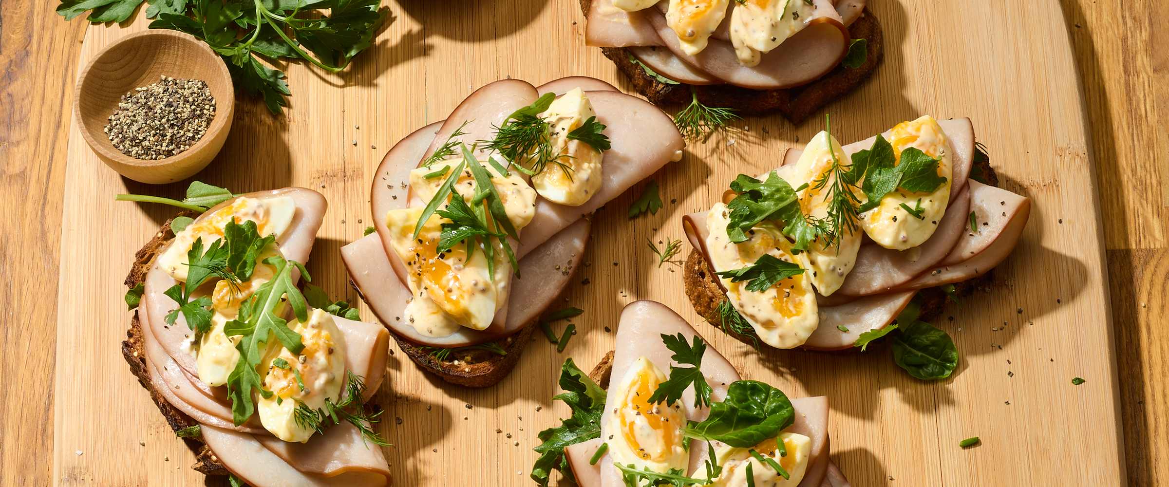 Open sandwiches with sliced turkey, eggs, and fresh herbs on a wooden cutting board.