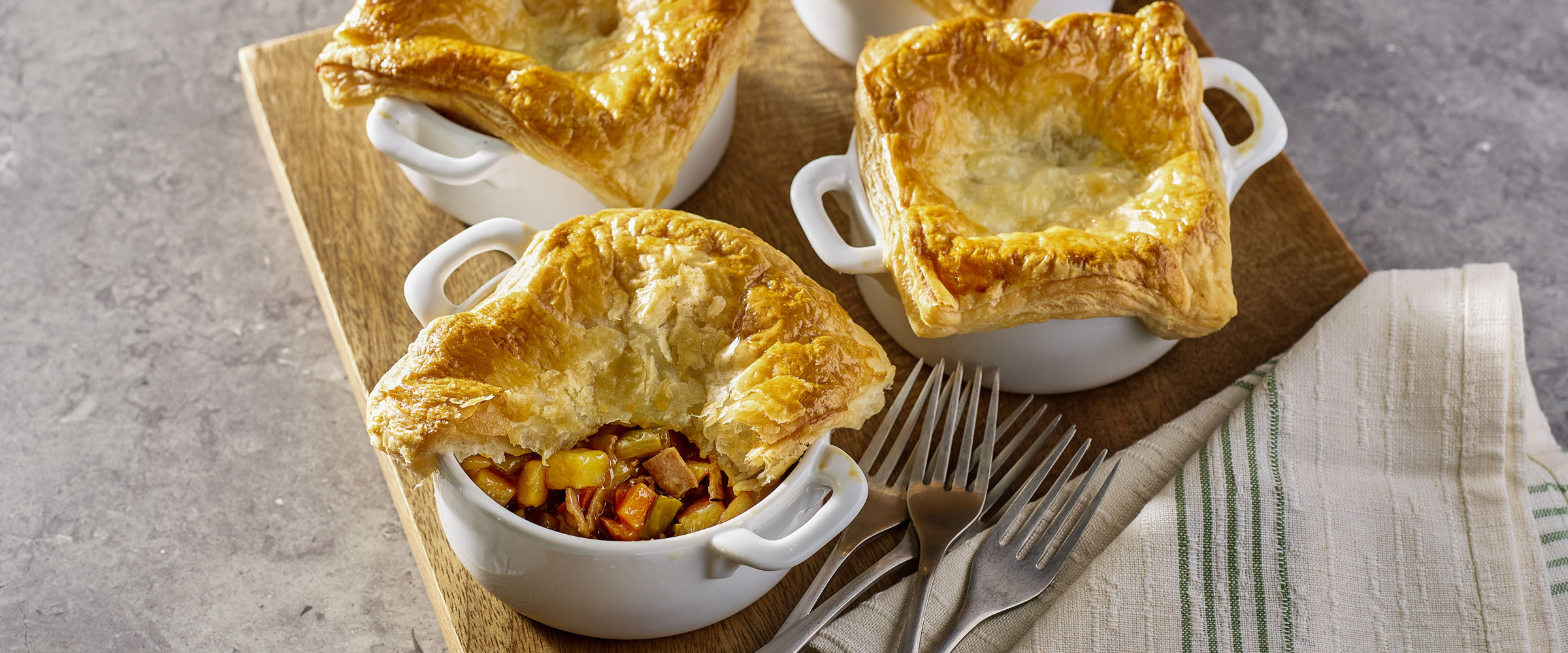 Four individual pot pies with golden-brown puff pastry tops on a light-colored countertop, served in white ceramic ramekins.